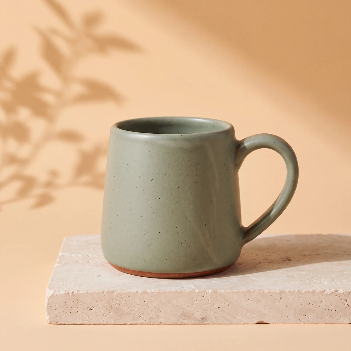 The reference mug reimagined on a limestone plinth with an apricot backdrop and soft leaf shadows